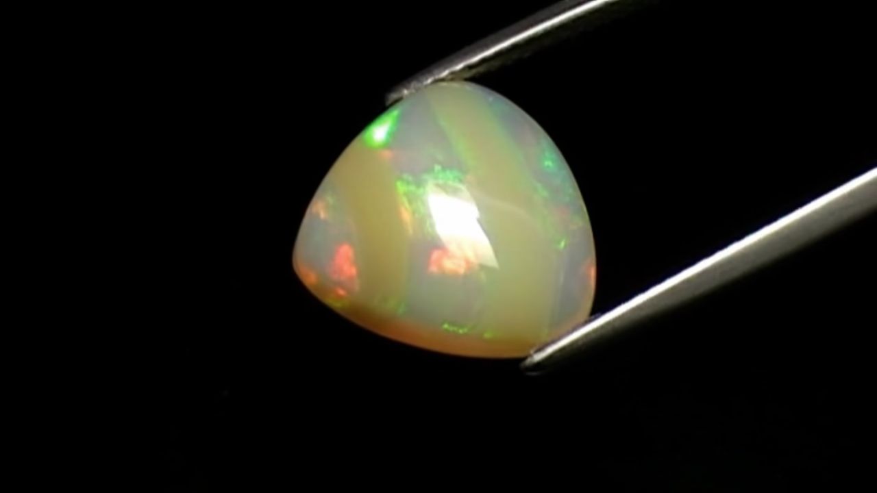 A pale opal displaying green, red, gold, and blue play-of-color.