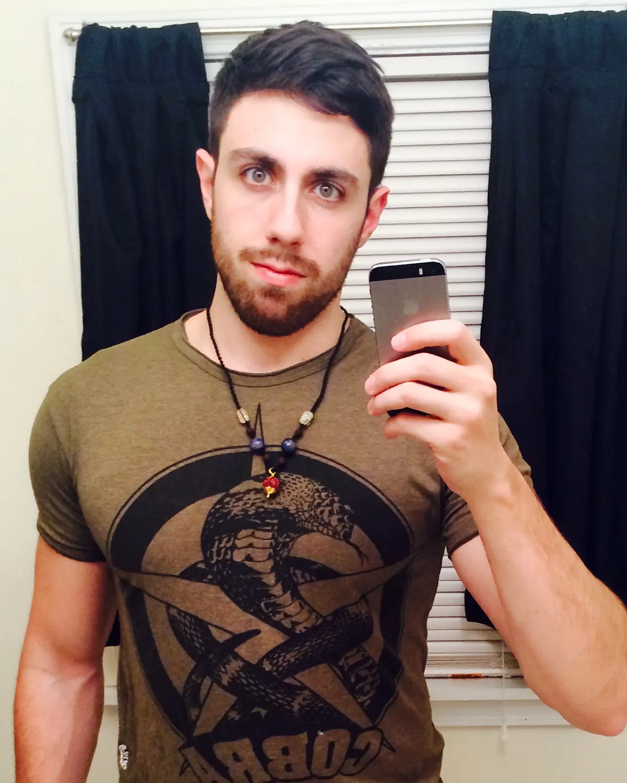 Mirror selfie of the author wearing an olive graphic tee with a snake design.